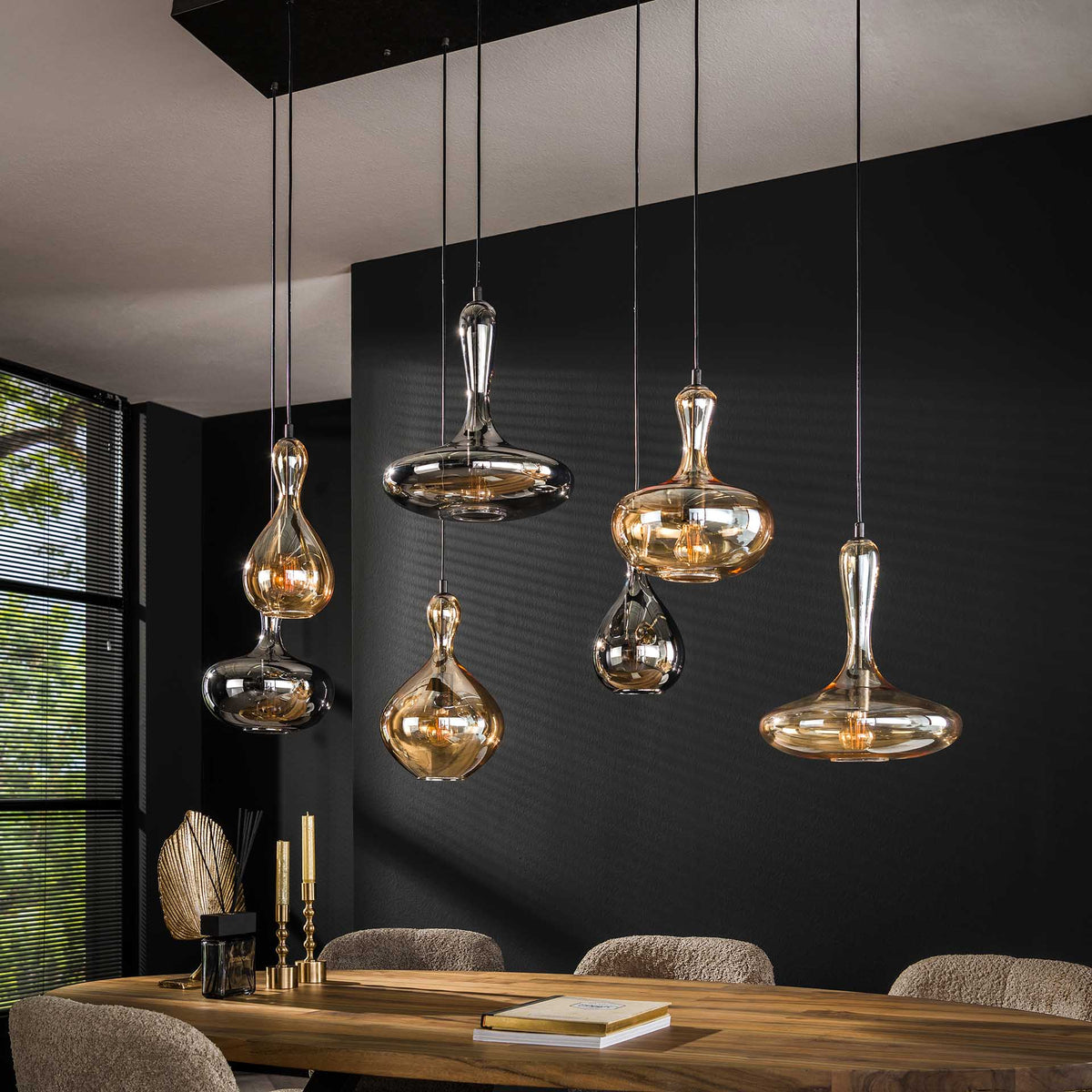 Pendellamper med ravfarvede glasskærme over et spisebord i træ, et eksempel på en designlampe, man kan følge prisen på