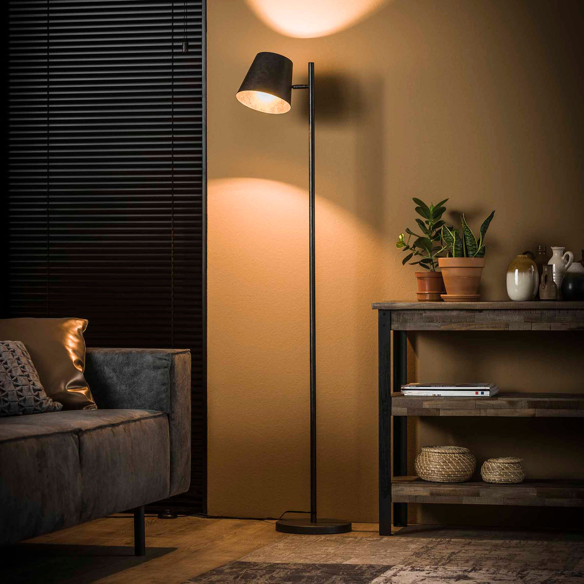Hygge i hjemmet: stue i varmt lys fra en gulvlampe med sofa, puder, grønne planter og kurve på en reol