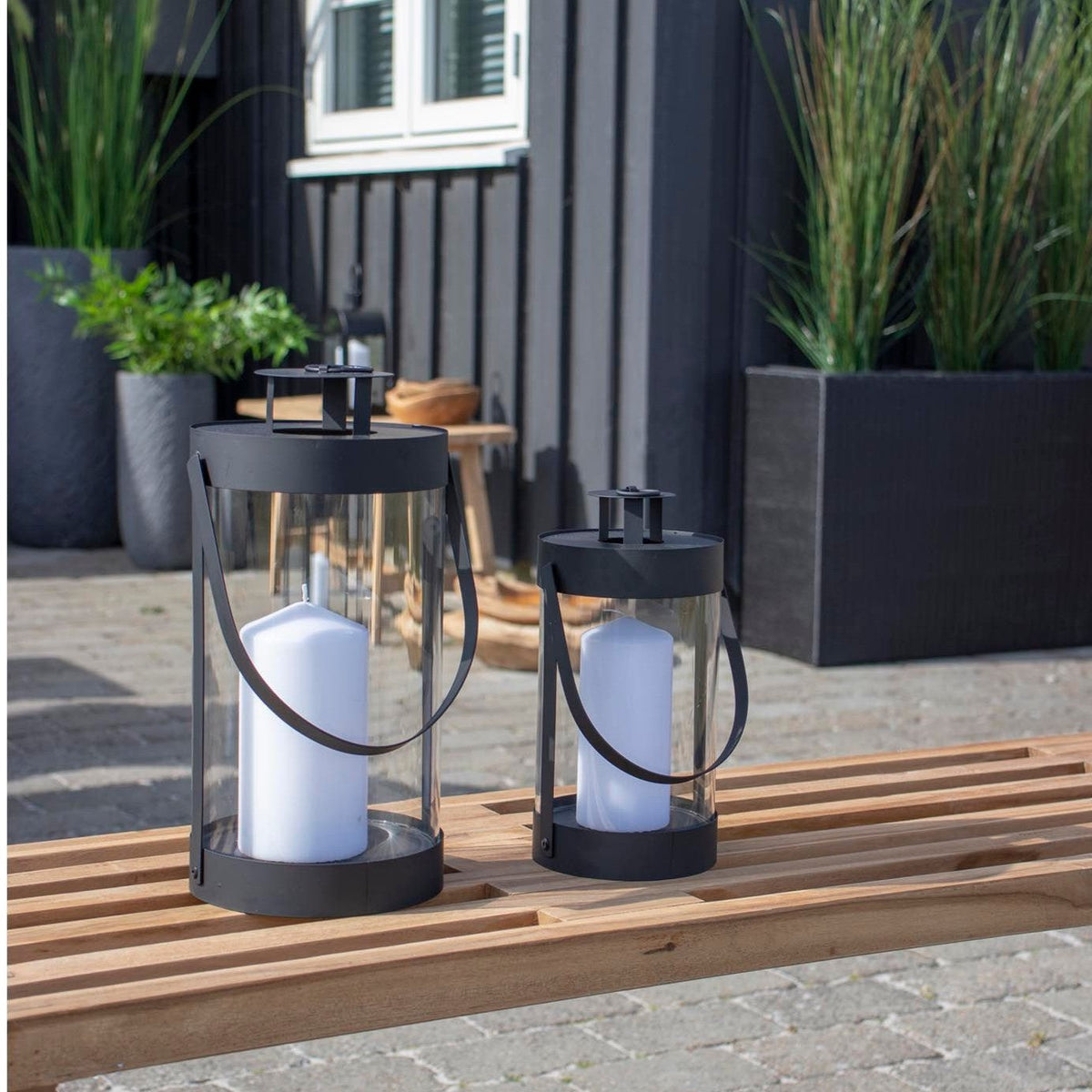 Terrasse med fliser og bænk foran et sortbejdset træhus med hvide vinduer